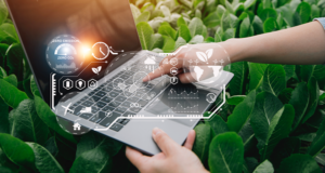 Uma mão segura um laptop sobre uma plantação, enquanto a outra digita. Acima aparecem gráficos de análise de dados do agronegócio.